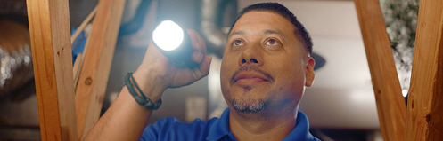 Stan's HVAC employee inspecting basement with a flashlight