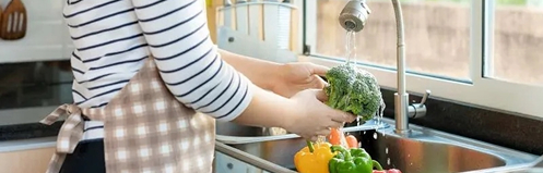 Woman washing produce in her kitchen sink