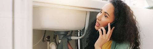 Woman holding towel on a leaky drain while on the phone with a plumber